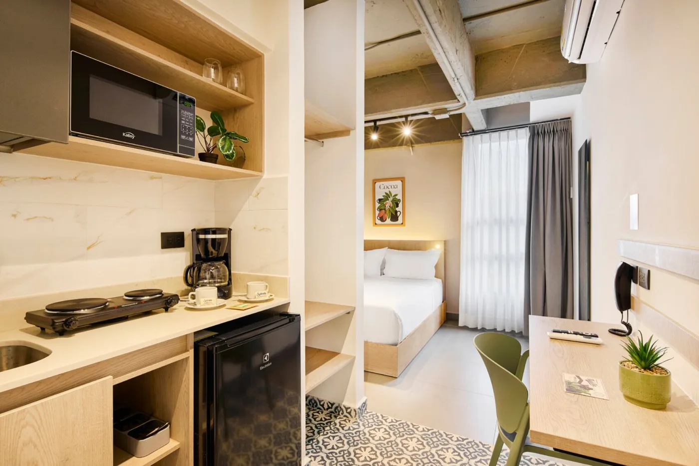 Cocineta con estufa, microondas, cafetera y minibar, con la cama al fondo