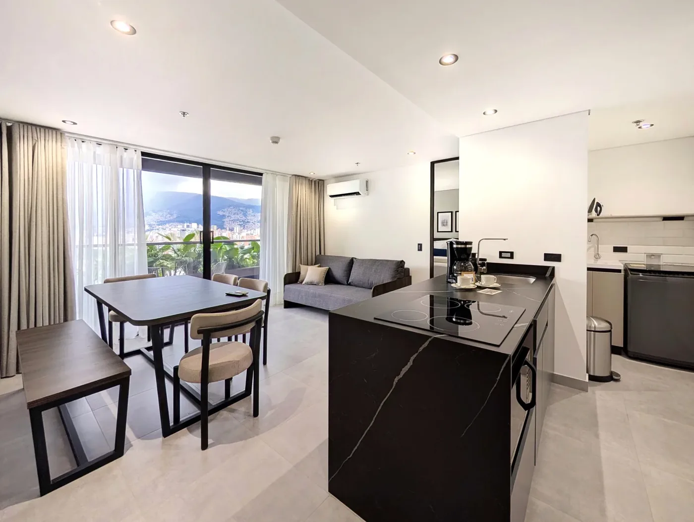 Sala-comedor de una suite con cocina equipada, isla de mármol negro y balcón con vista