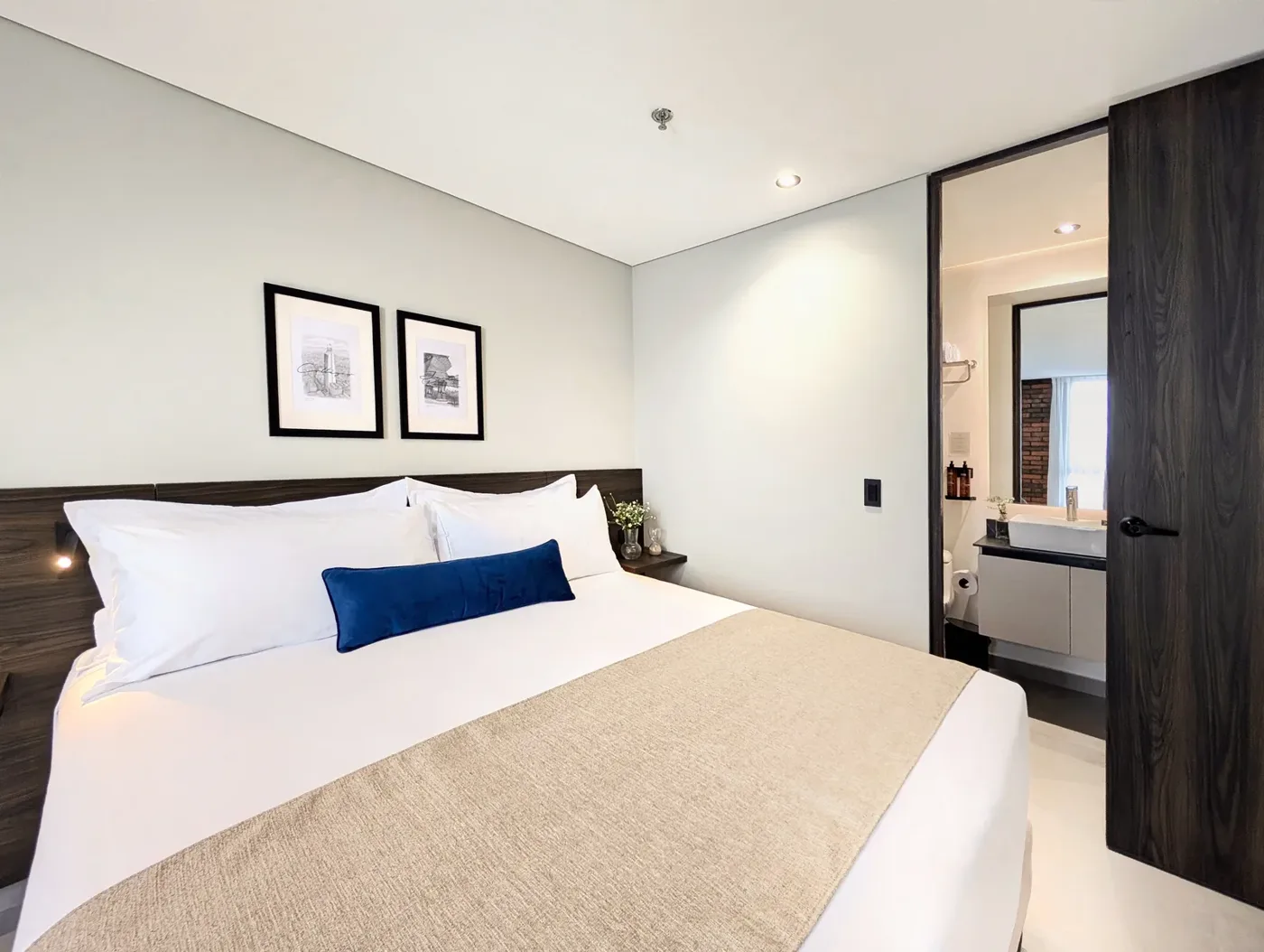 Dormitorio con cama king, cuadros en blanco y negro y baño al fondo