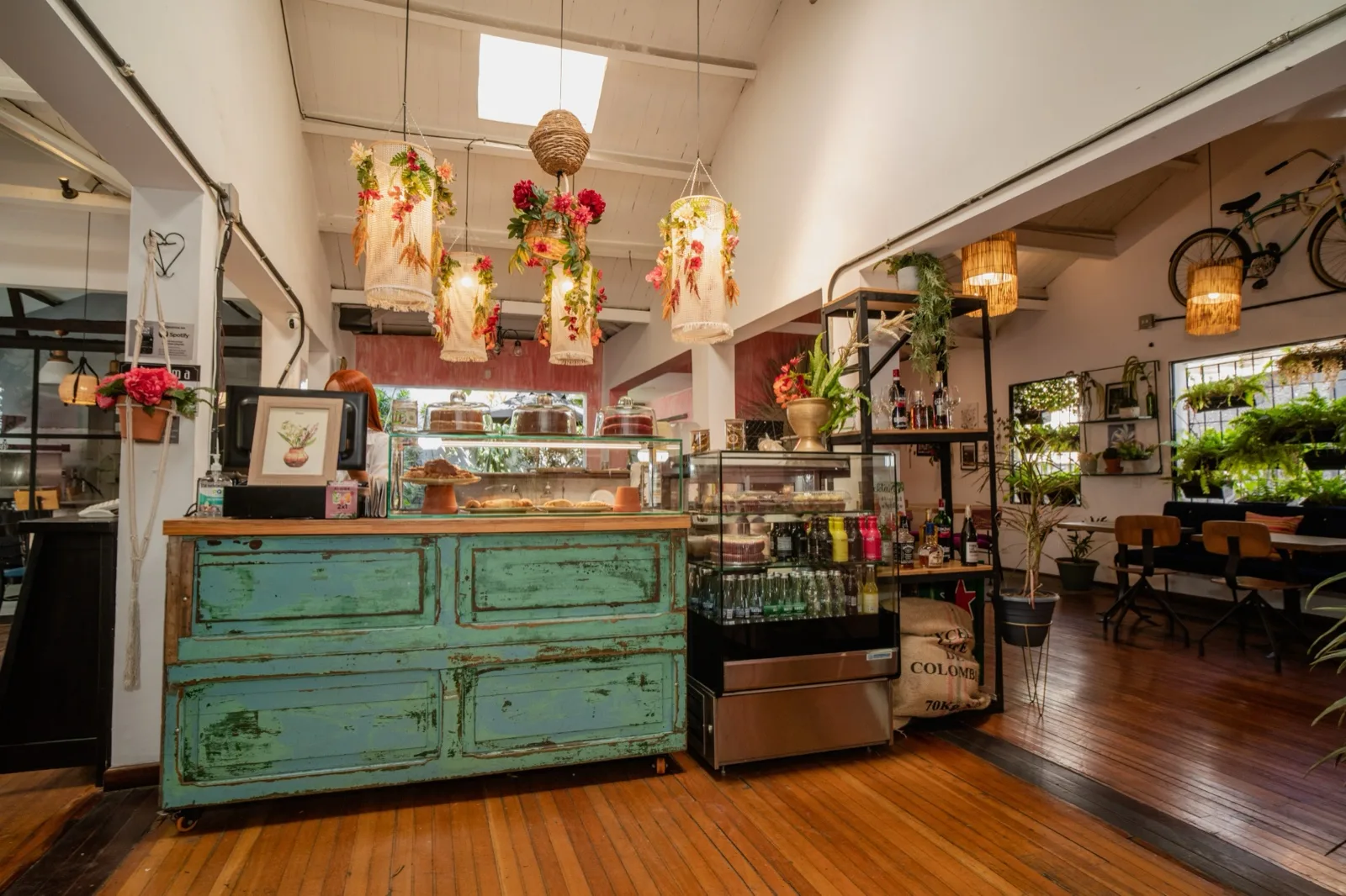Mostrador verde antiguo con tortas en vitrina y lámparas con flores en un local de Al Alma