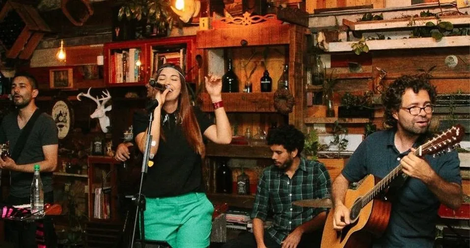 Banda tocando en vivo en Alambique, entre estantes de madera con libros y botellas