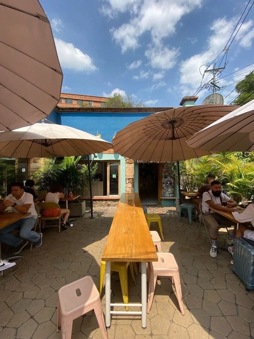 Patio de Betty's Bowls con mesa larga de madera, butacos rosados y sombrillas