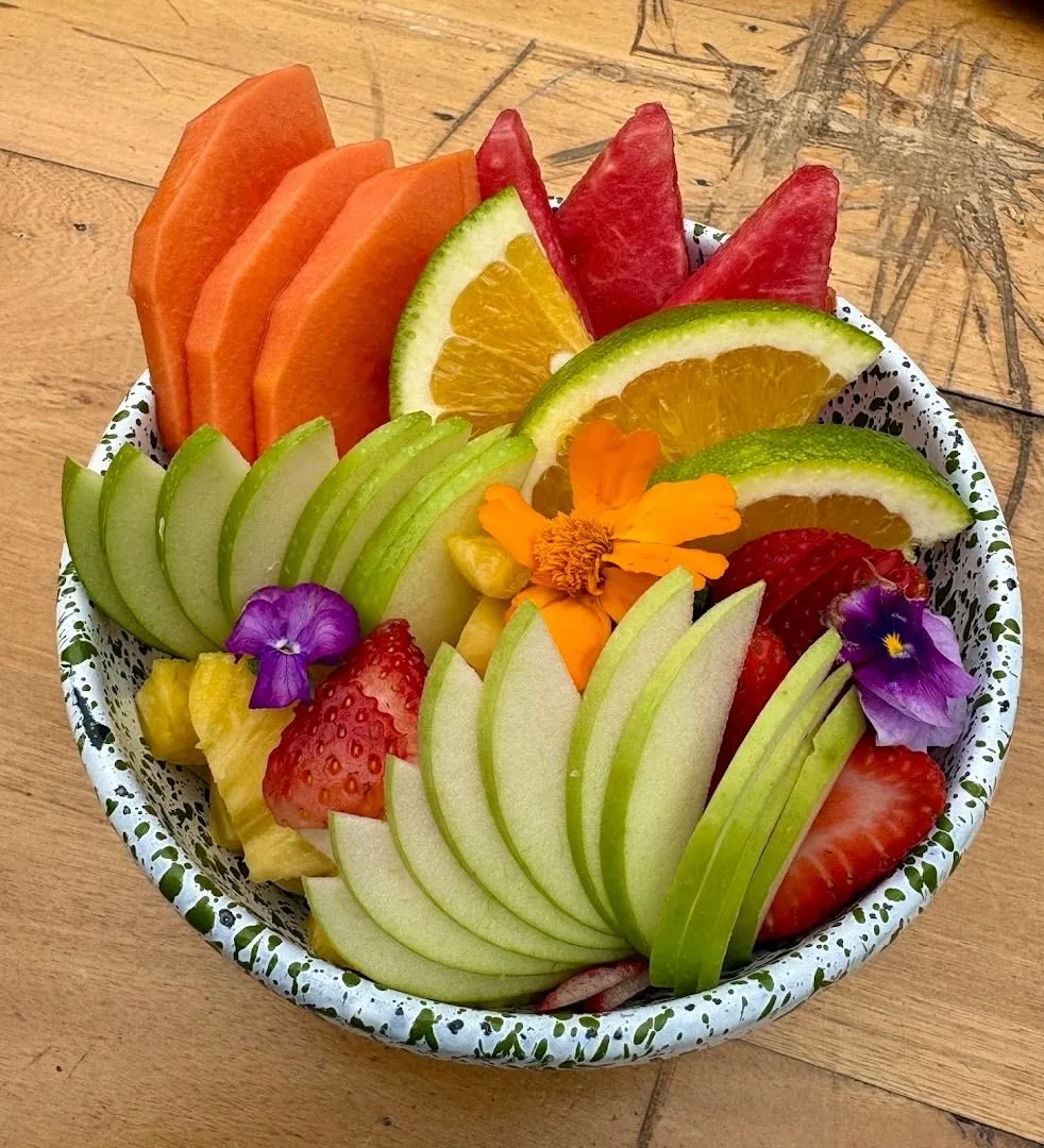 Bowl de papaya, manzana verde, fresas, mandarina y flores en plato de peltre