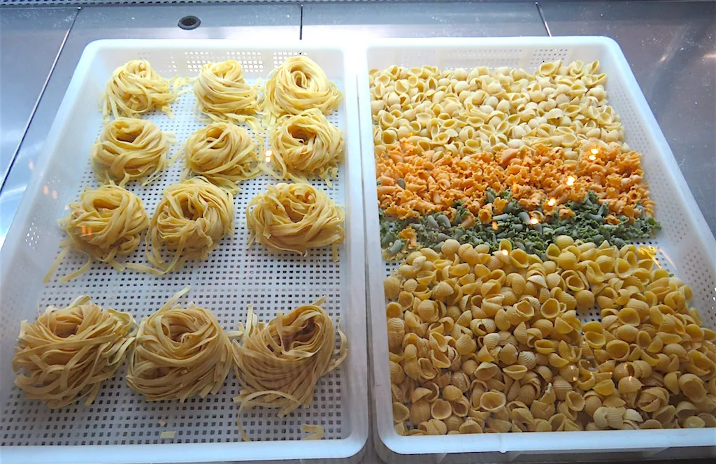 Nidos de pasta fresca y conchitas de colores en bandejas en la cocina de Caduff