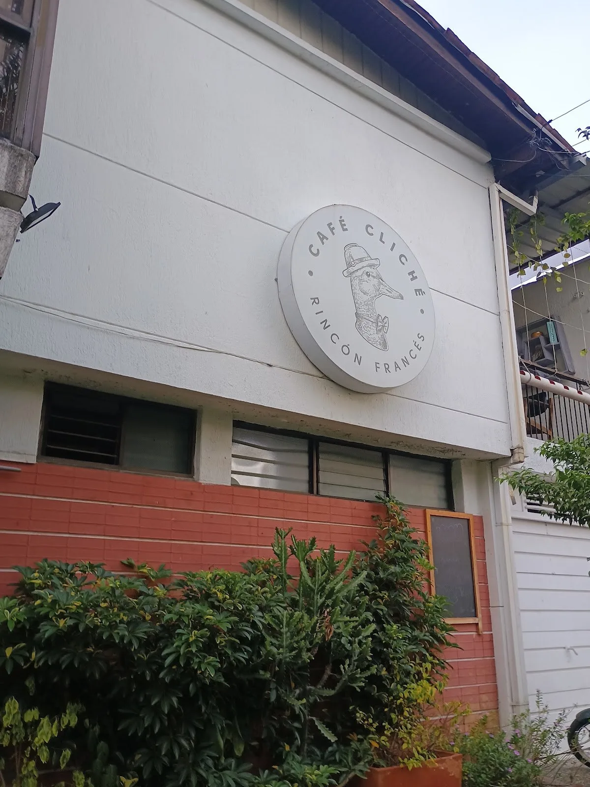 Fachada de la casa de Café Cliché con su letrero redondo y jardinera