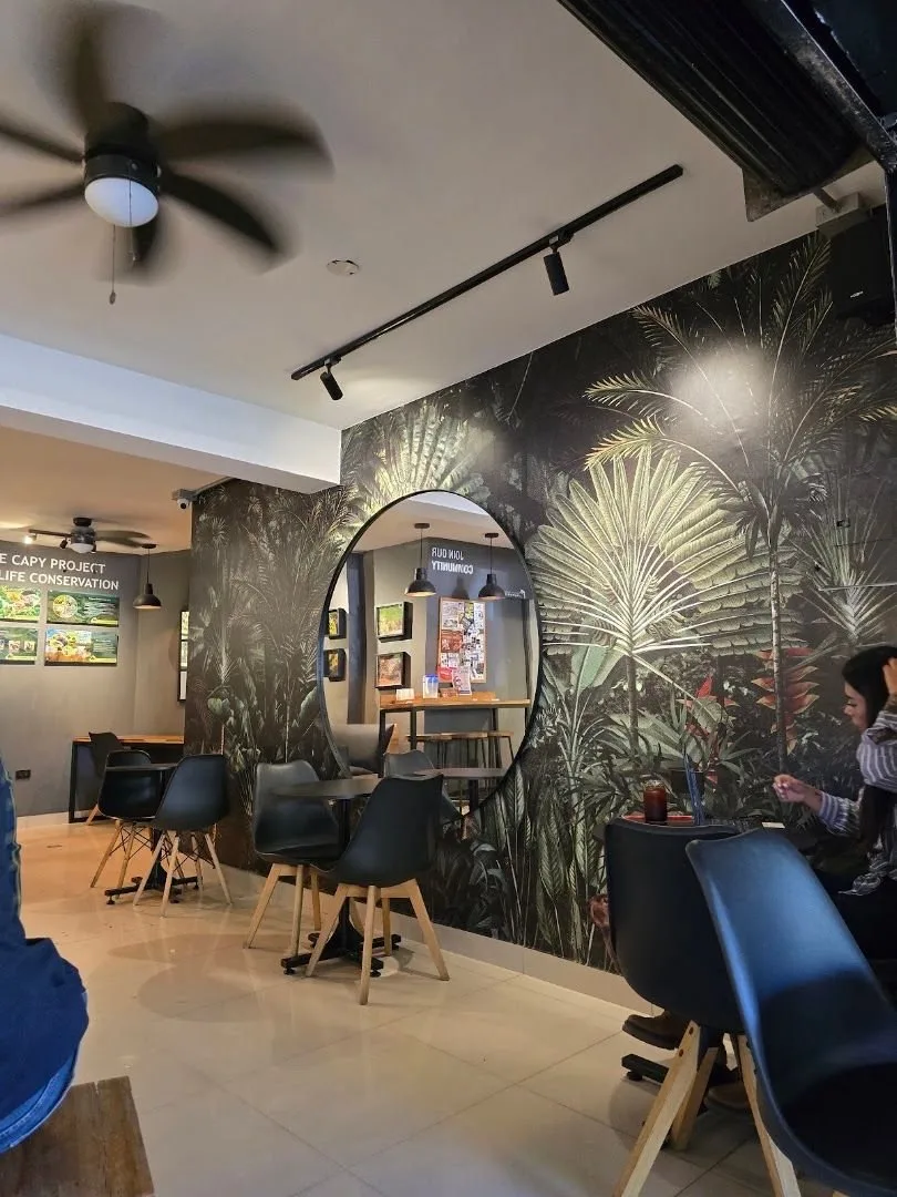 Interior de Café Revolución con pared de hojas tropicales, espejo redondo y mesas pequeñas