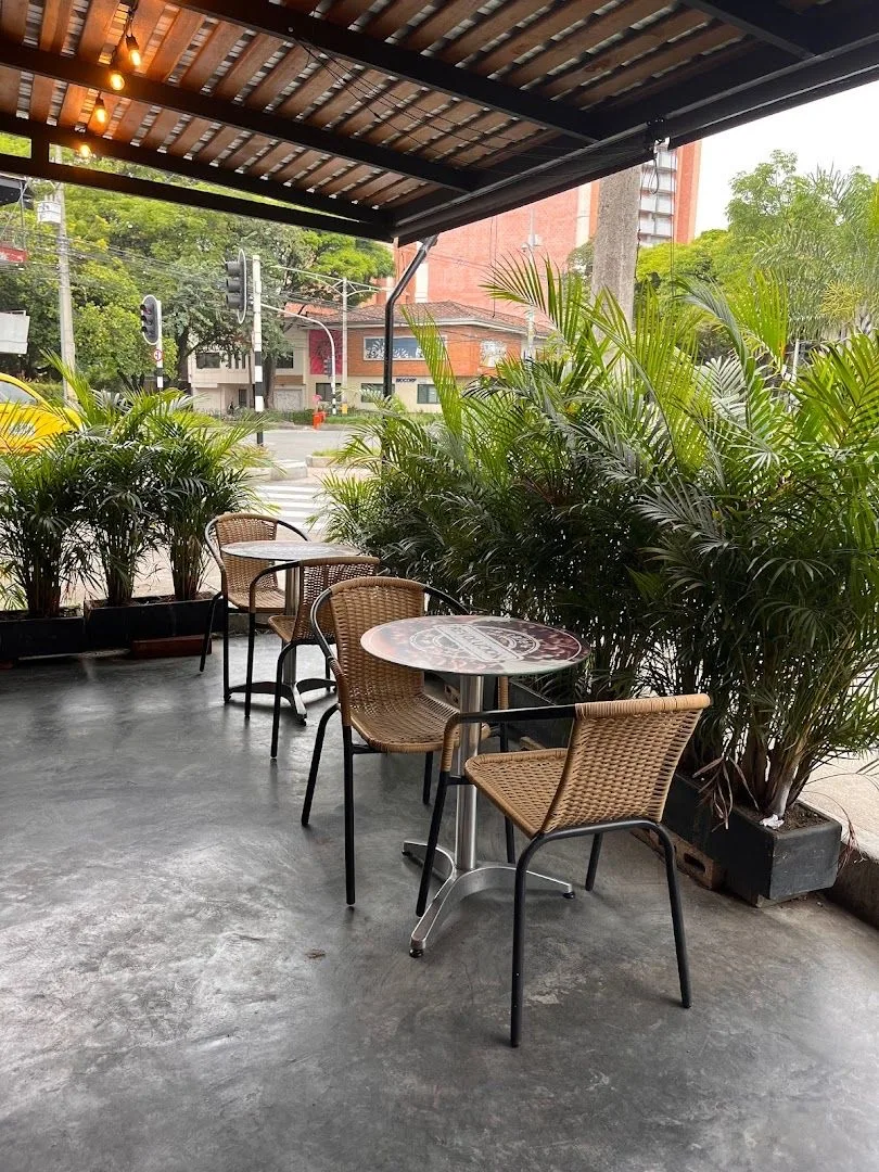 Terraza de Café Revolución con mesas de mimbre bajo pérgola y palmas
