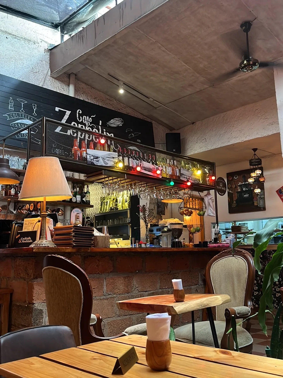 Barra de Café Zeppelin con letrero en tablero, botellas, luces de colores y una lámpara de pie