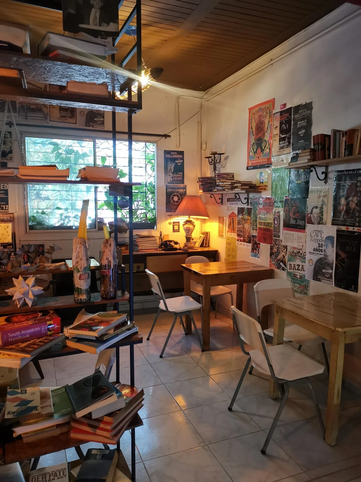 Salón de Café Zeppelin con estantes de libros, afiches en la pared y una lámpara encendida