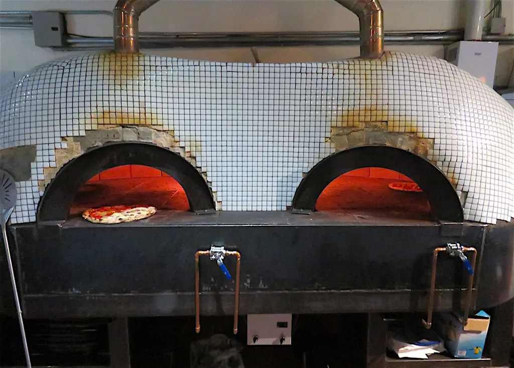 Dos hornos de leña encendidos con baldosa blanca en la cocina de Café Zorba