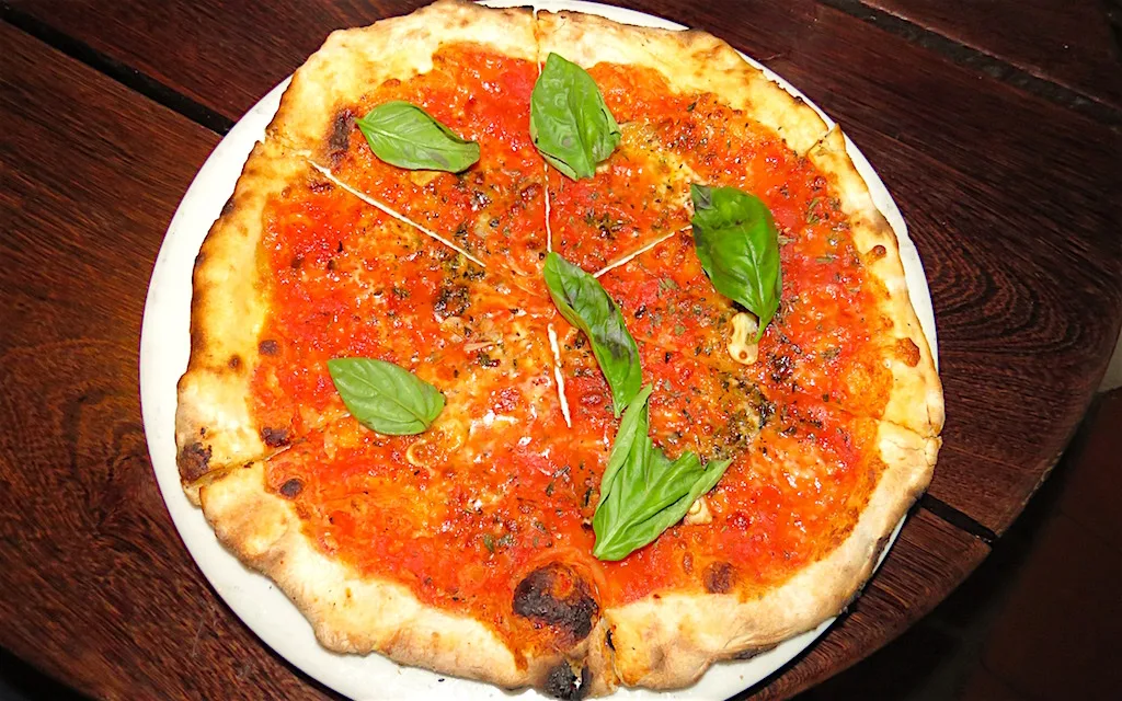 Pizza marinara de masa delgada con hojas de albahaca sobre una mesa de madera en Café Zorba