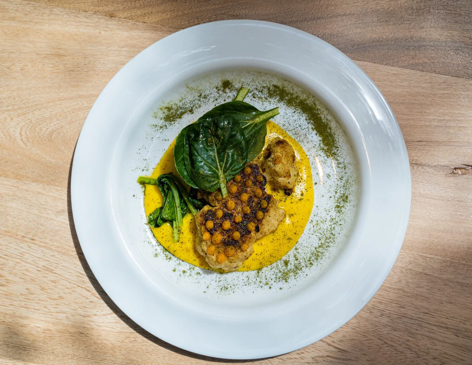Plato de pescado con salsa amarilla y hojas verdes en Carmen