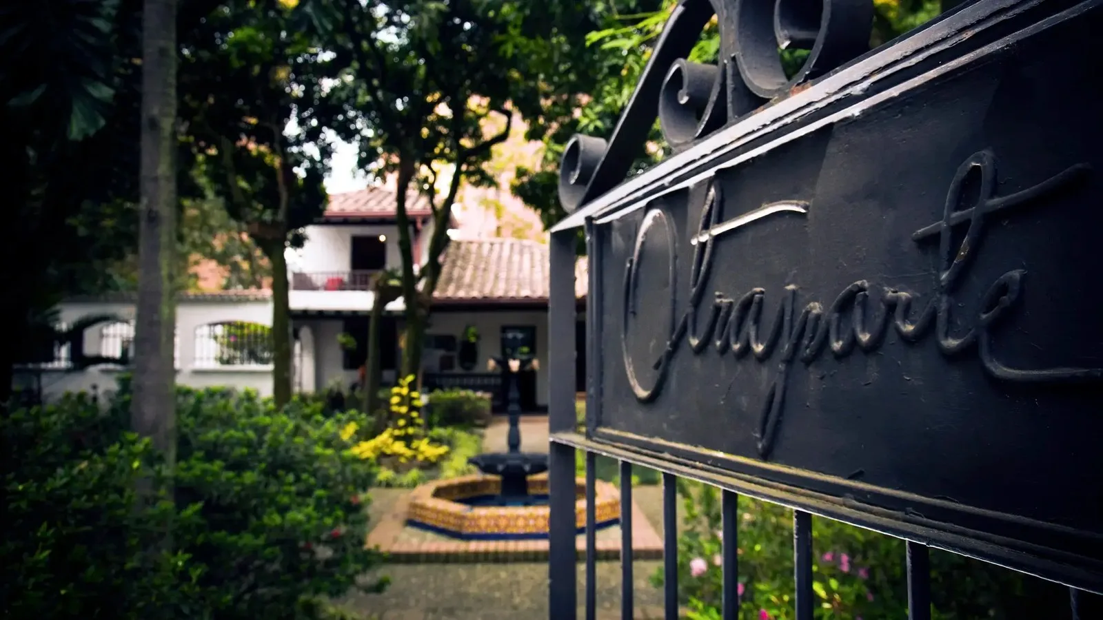 Reja de entrada con el nombre Otraparte y el jardín de la casa de Fernando González