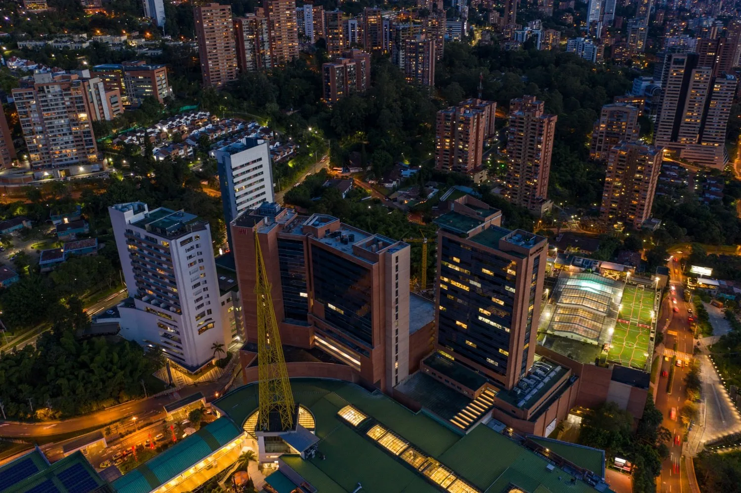 Vista aérea de El Tesoro Parque Comercial al anochecer, entre los edificios de la loma