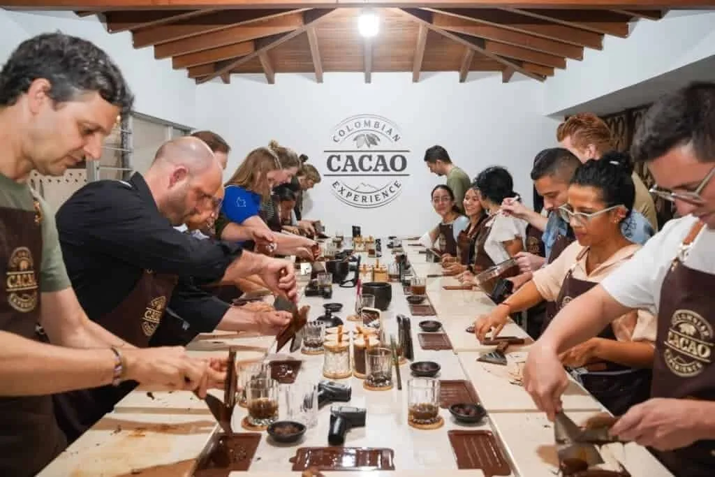 Grupo trabajando el chocolate en una mesa larga bajo un techo de madera con el logo del taller