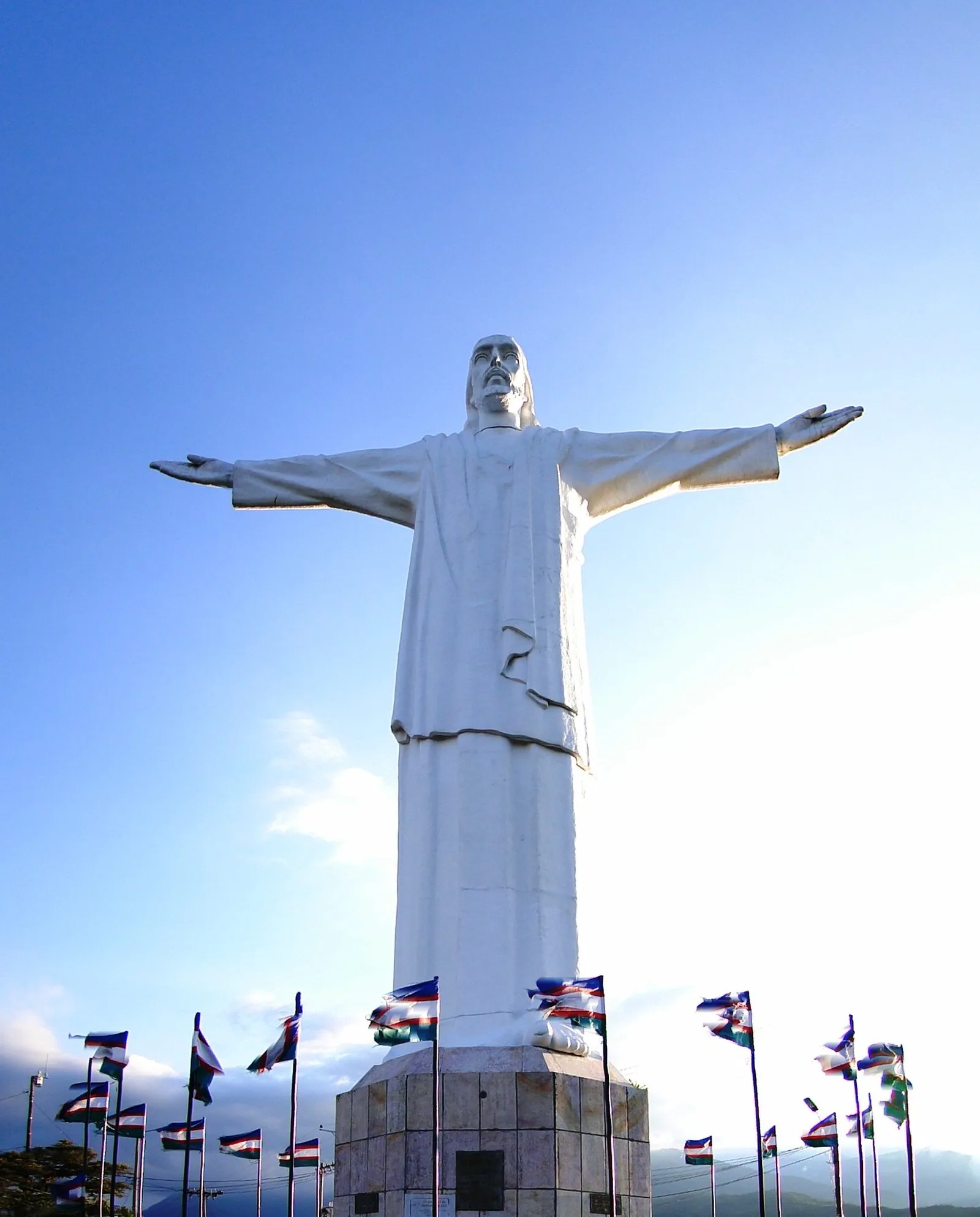 Estatua del Cristo Rey contra el cielo azul, con banderas al pie