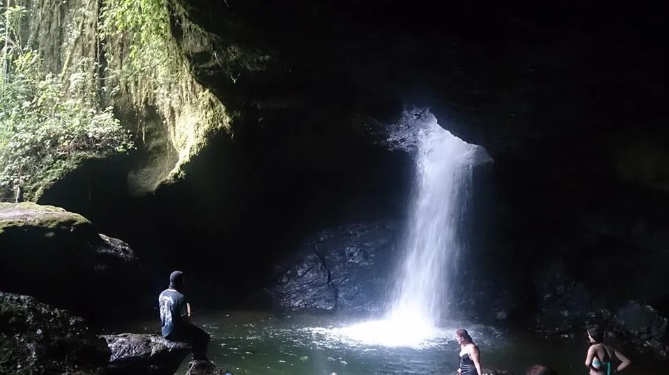 Bañistas en el pozo dentro de la cueva mientras la cascada entra por la abertura iluminada