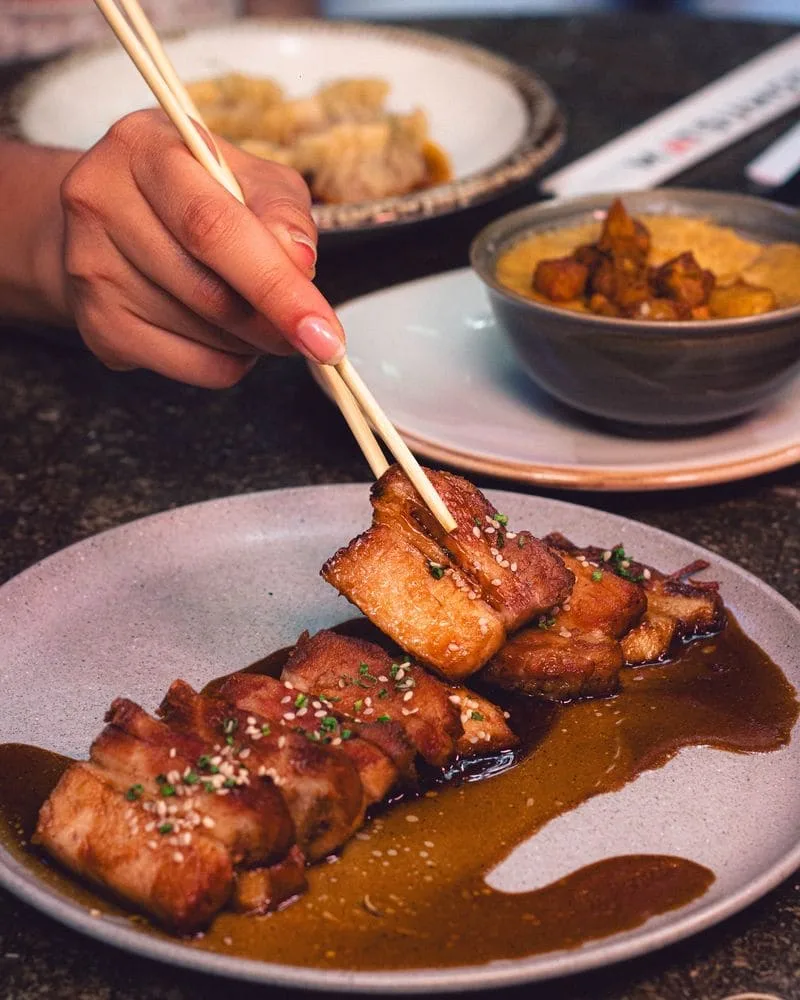 Panceta de cerdo glaseada al estilo coreano servida en Cuon, tomada con palillos