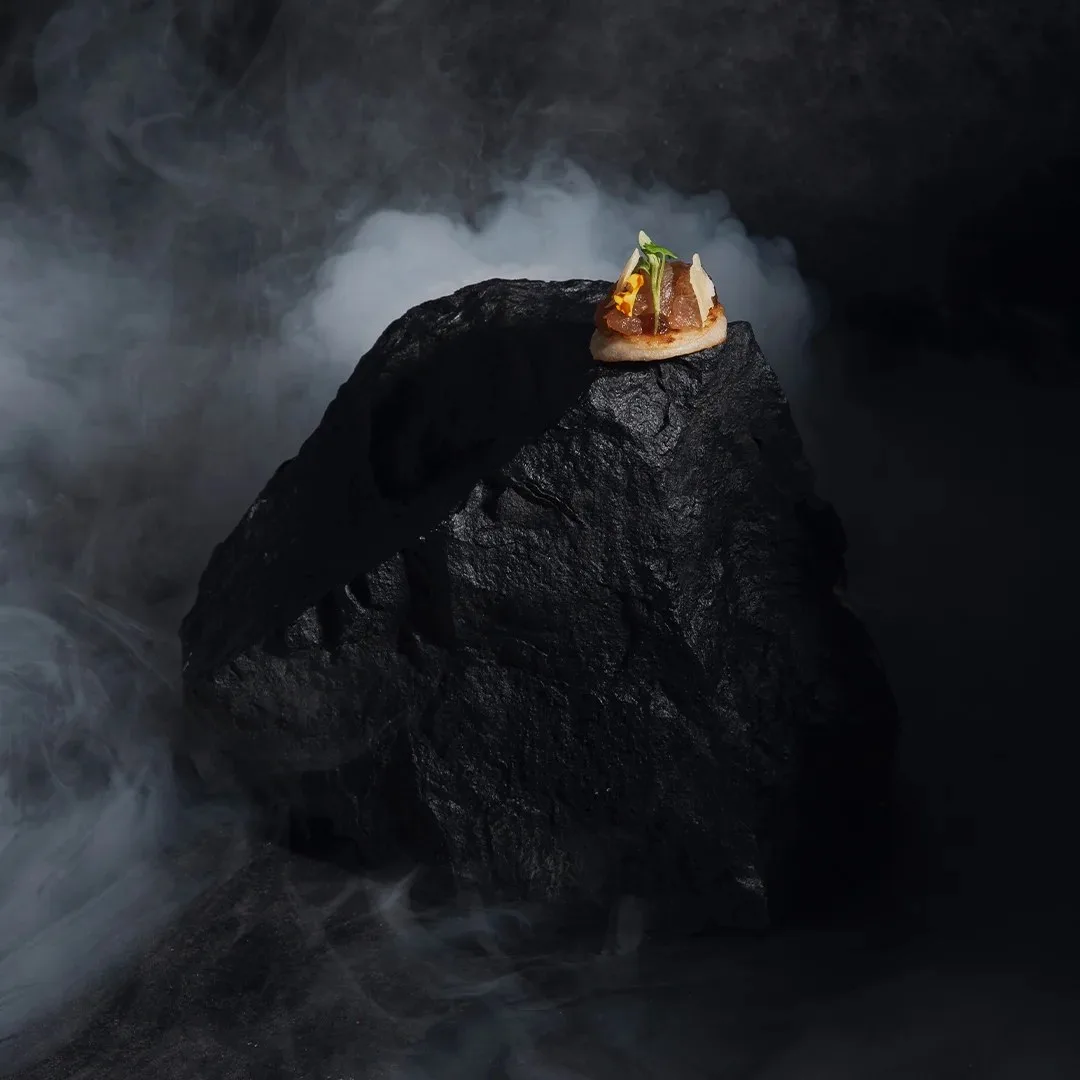 Bocado servido sobre una piedra negra con humo, del menú de El Cielo