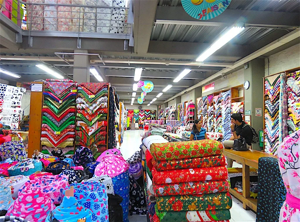 Rollos de telas estampadas de colores apilados dentro de un almacén de El Hueco