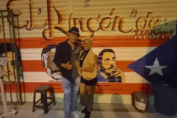 Pareja frente al mural con el nombre de El Rincón de Heberth
