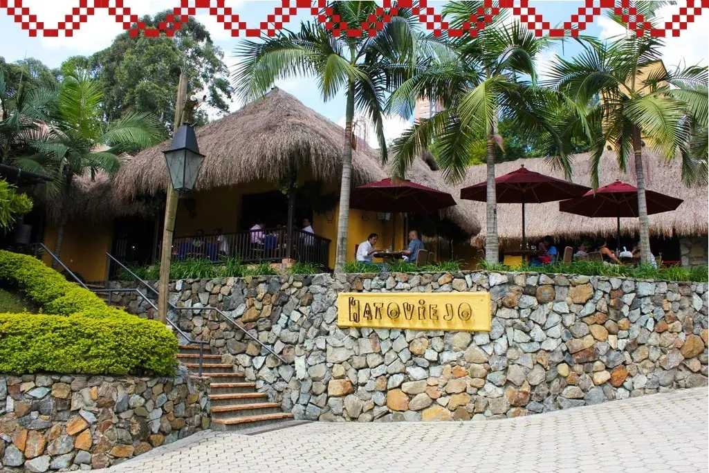 Entrada de Hatoviejo con techos de paja, palmeras y muro de piedra