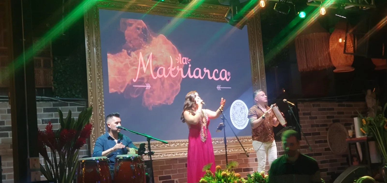 Cantante de vestido fucsia con percusionista y acordeonista en la tarima de La Matriarca