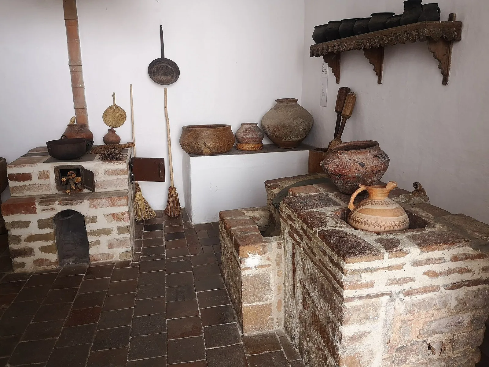 Cocina antigua del museo con fogones de ladrillo, ollas de barro y utensilios colgados en la pared