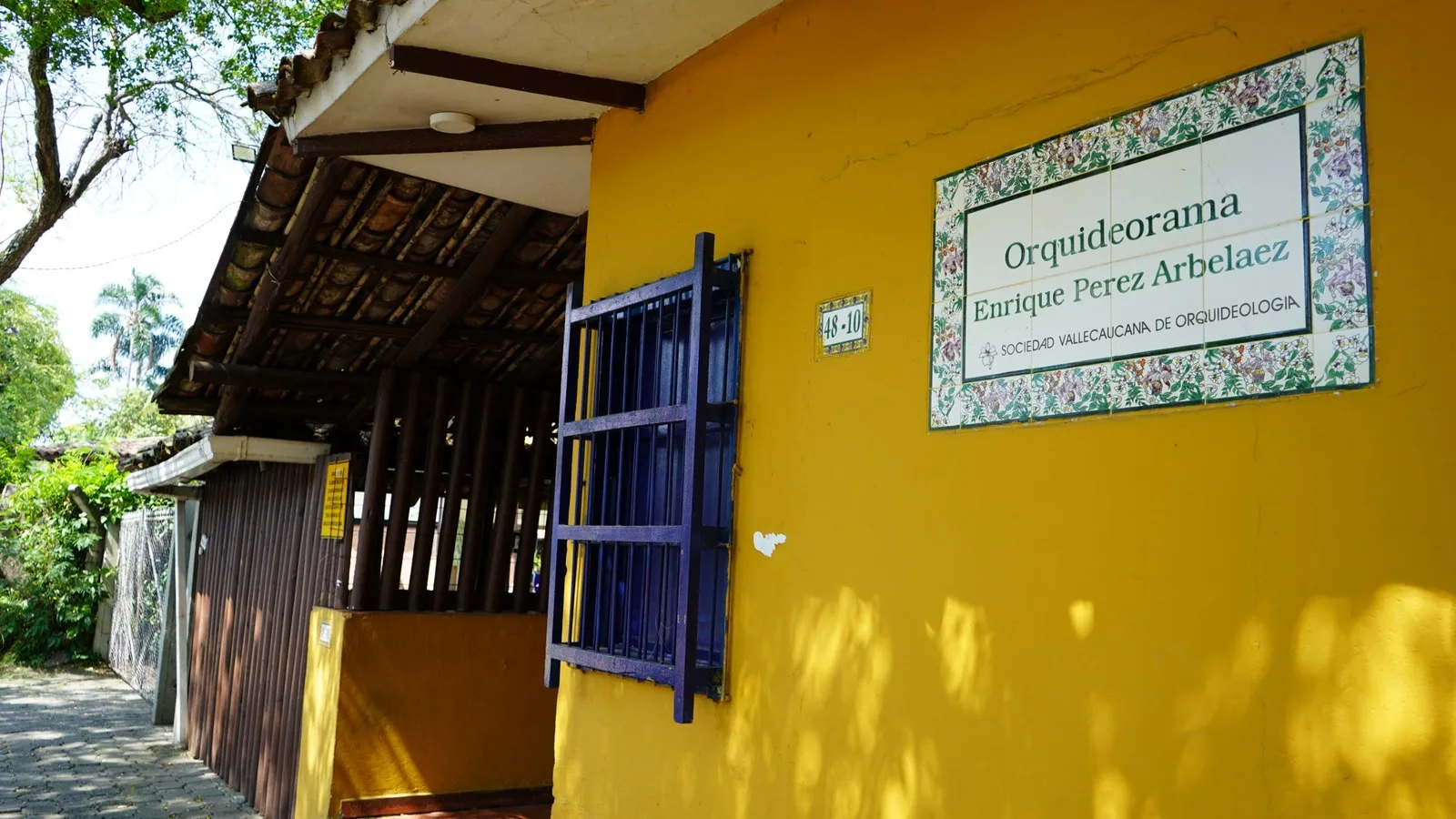 Entrada amarilla del Orquideorama Enrique Pérez Arbeláez con su placa de azulejos