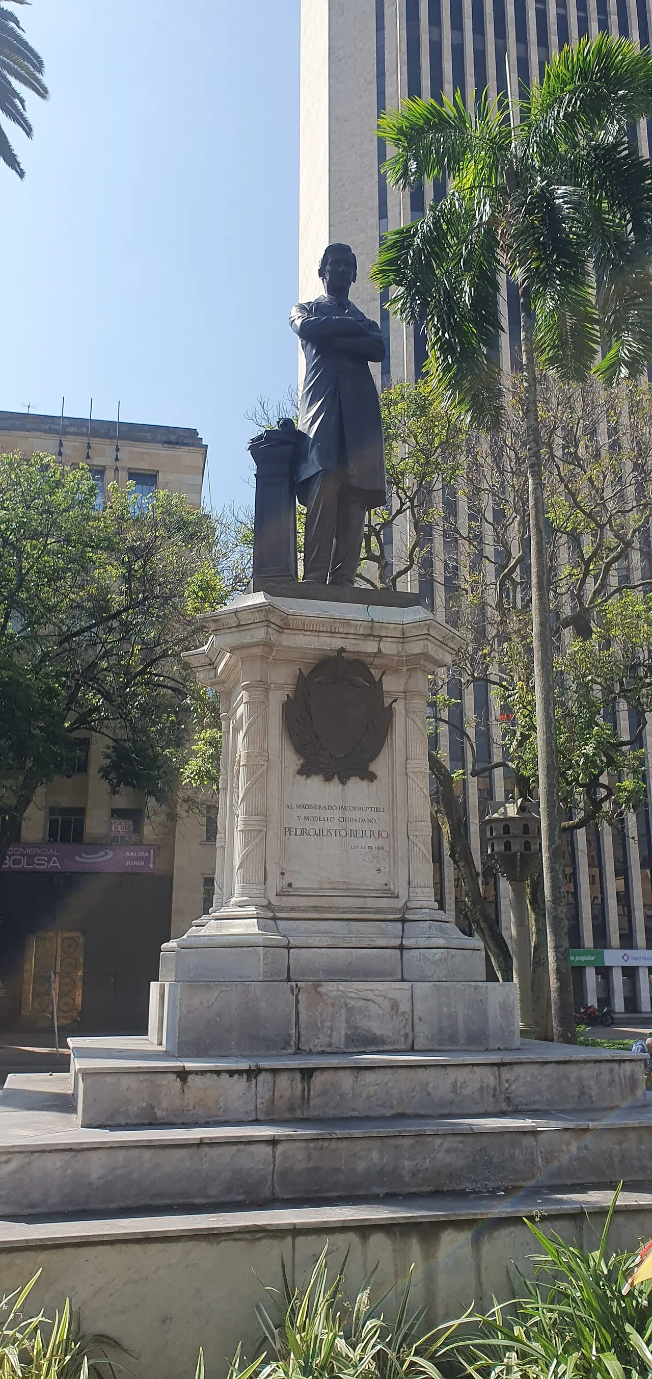 Estatua de bronce de Pedro Justo Berrío sobre su pedestal de mármol, rodeada de palmas y edificios