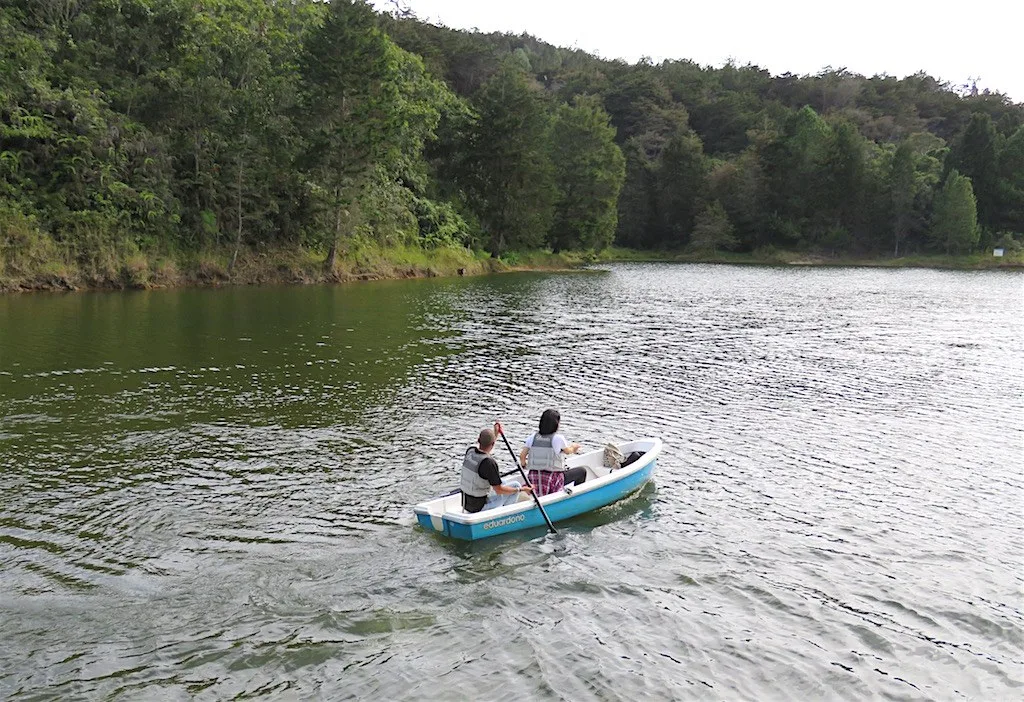 Dos personas remando en un bote por el lago de Piedras Blancas, con bosque alrededor