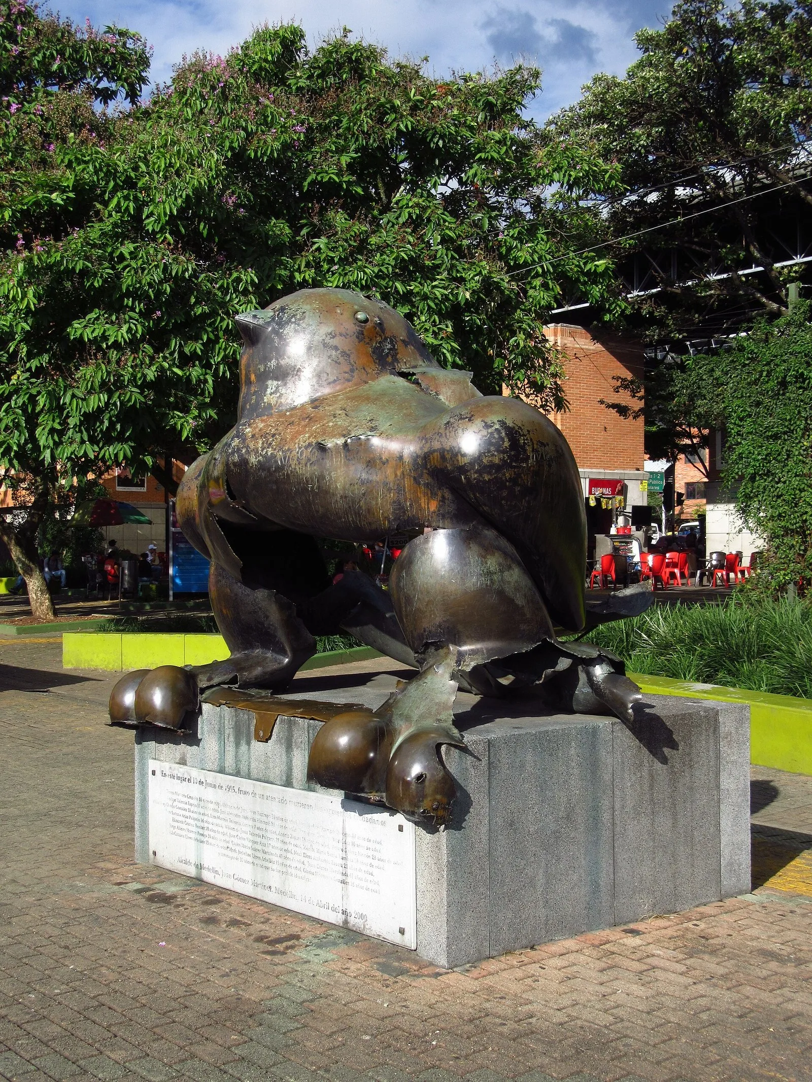 Escultura de bronce del pájaro de Botero abierta por la explosión, sobre su pedestal con la placa