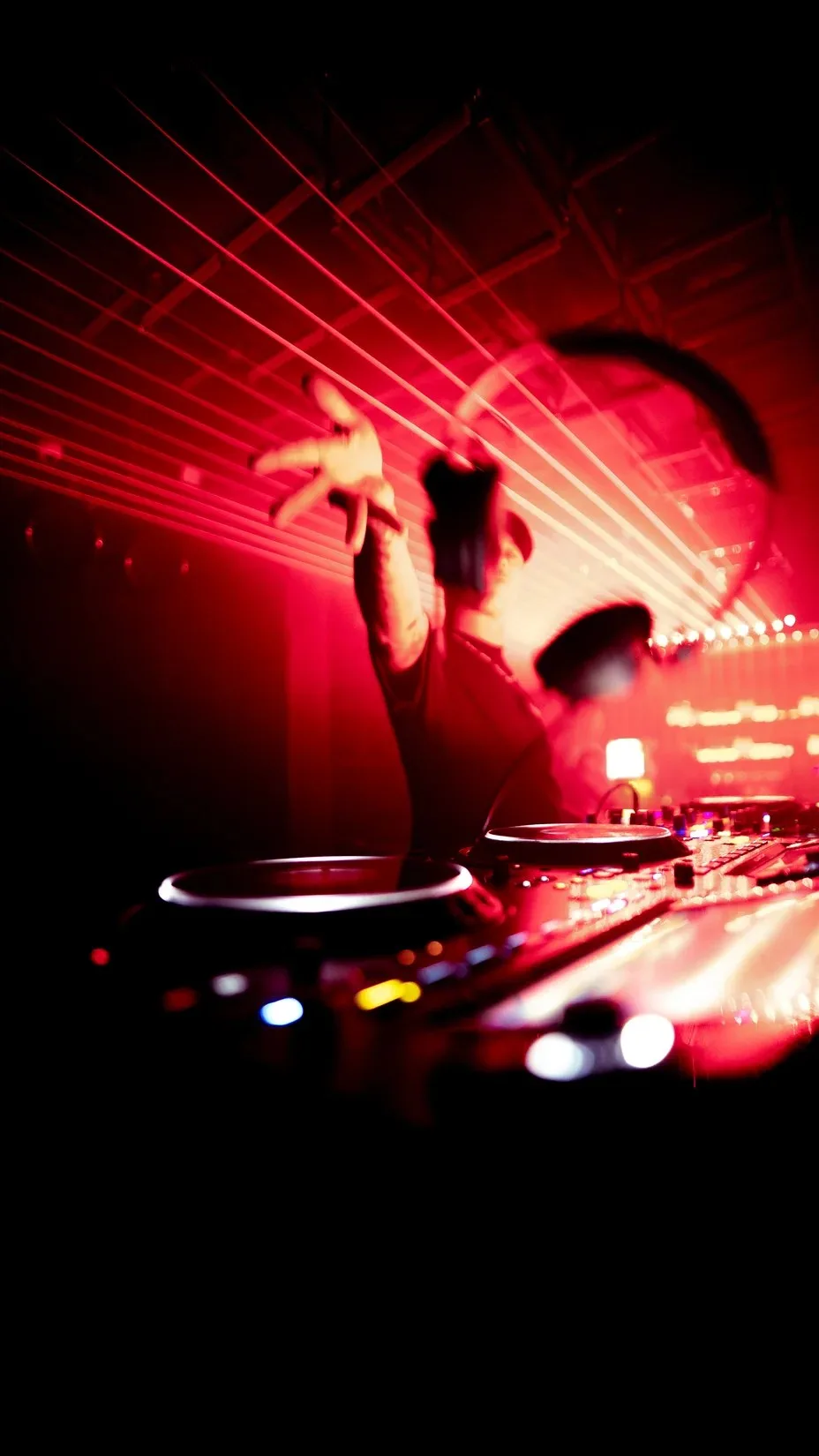 DJ con el brazo arriba frente a la consola, entre láseres rojos