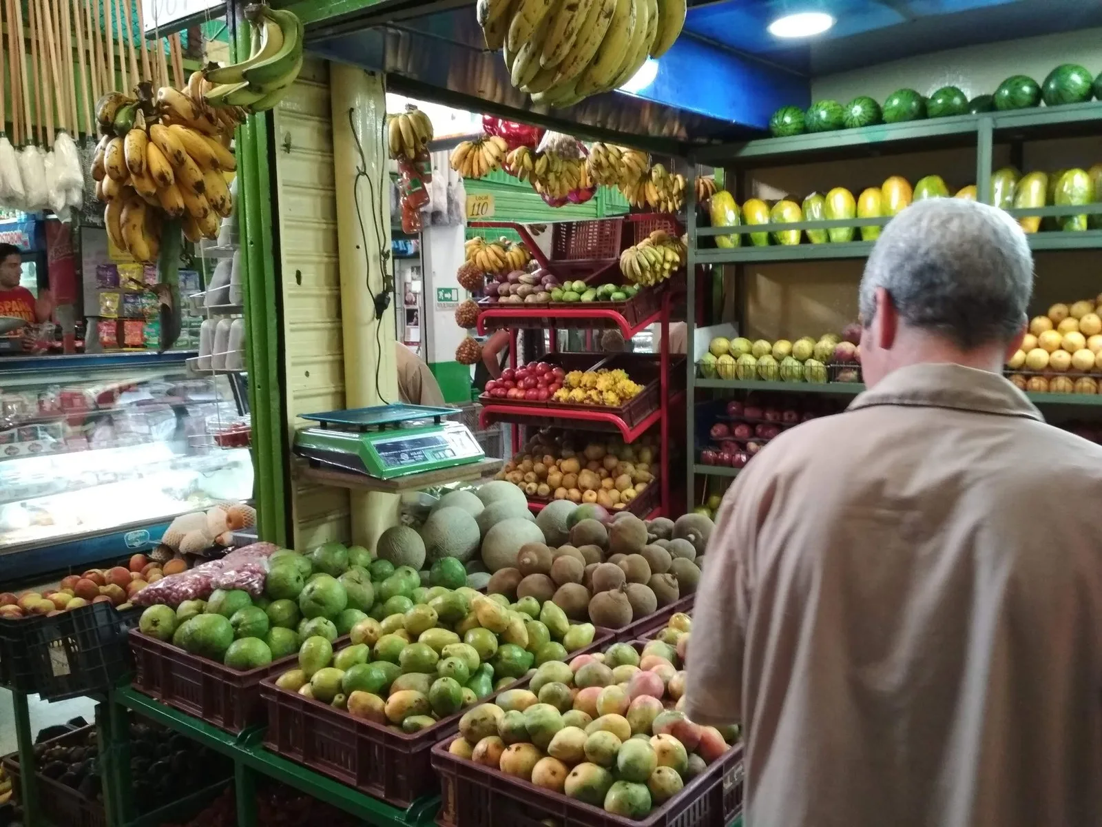 Puesto de frutas con mangos, papayas, sandías y racimos de banano colgados en la plaza de La América