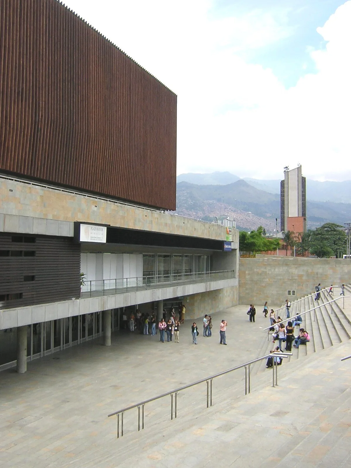 Entrada al centro de convenciones de Plaza Mayor, bajo el volumen de madera, con gente en las escaleras