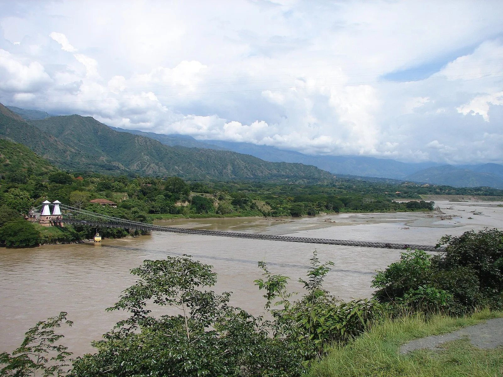 El Puente de Occidente completo sobre el río Cauca, visto desde una loma con montañas al fondo