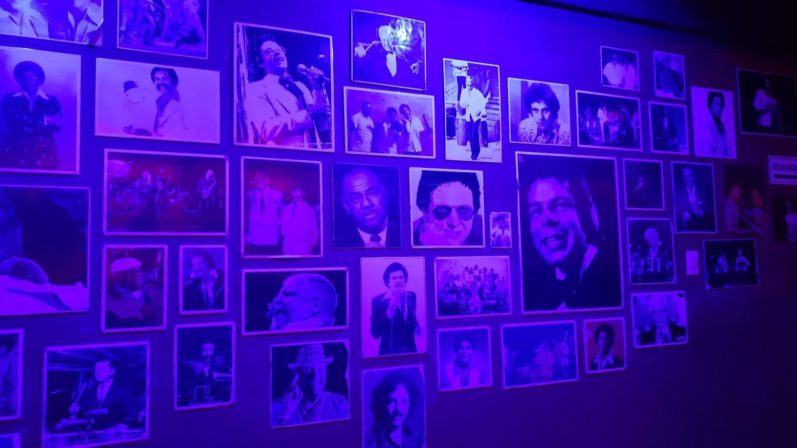 Pared de Punto Baré con fotos enmarcadas de músicos de salsa bajo luz morada