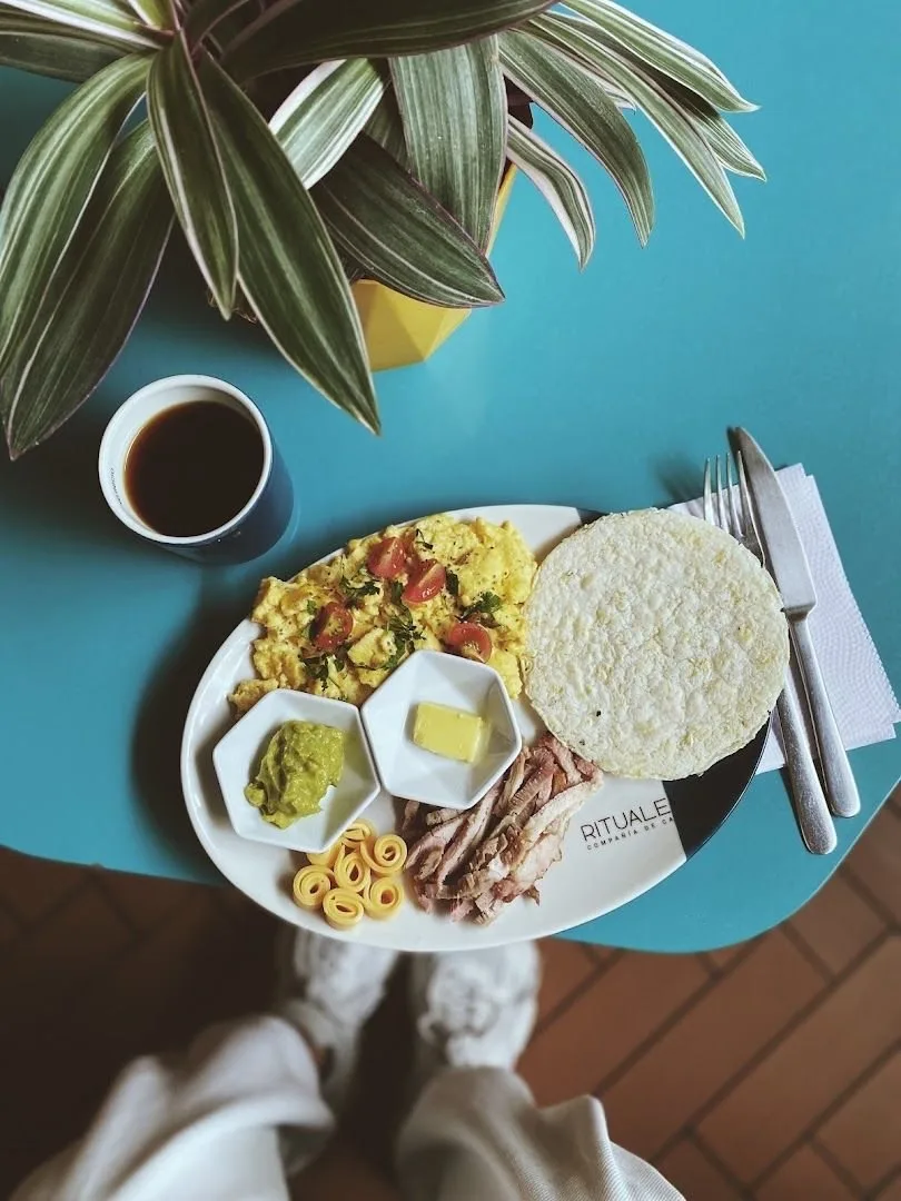 Desayuno de huevos pericos, arepa, carne, guacamole y café sobre mesa azul