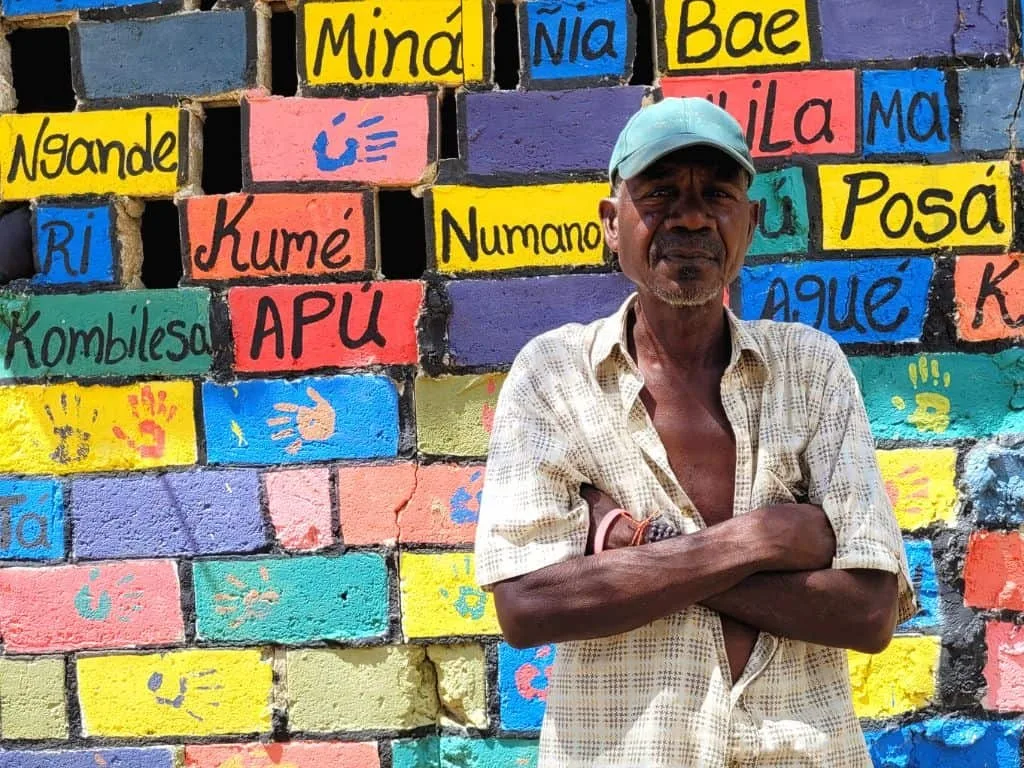Un habitante de Palenque frente a un muro pintado con palabras en lengua palenquera