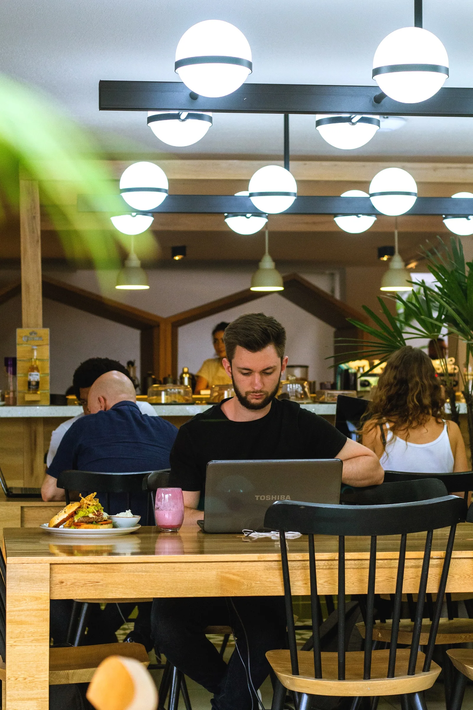 Hombre trabajando con portátil en una mesa del café de Semilla, bajo lámparas de globo