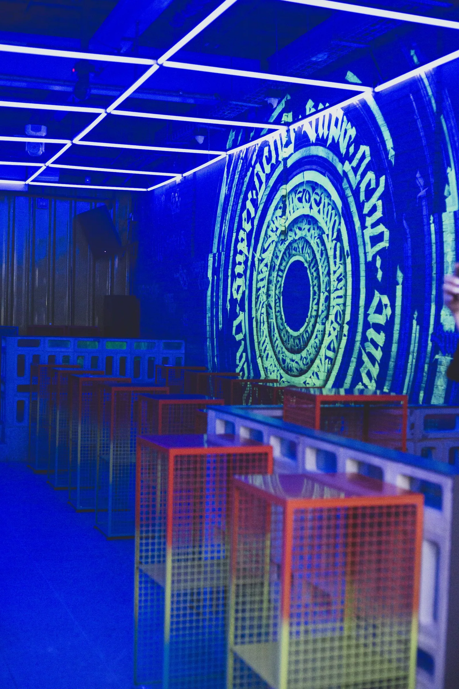 Sala Super 8 con luces azules, techo de neón y mesas de malla de colores
