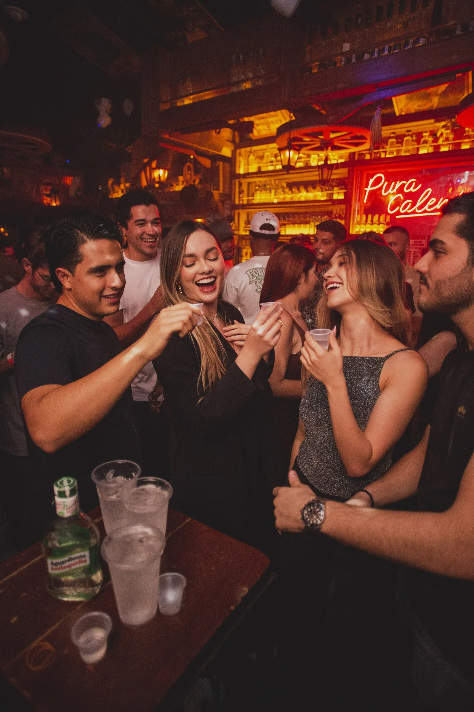 Grupo brindando con aguardiente frente a la barra de la sala 100 Fuegos