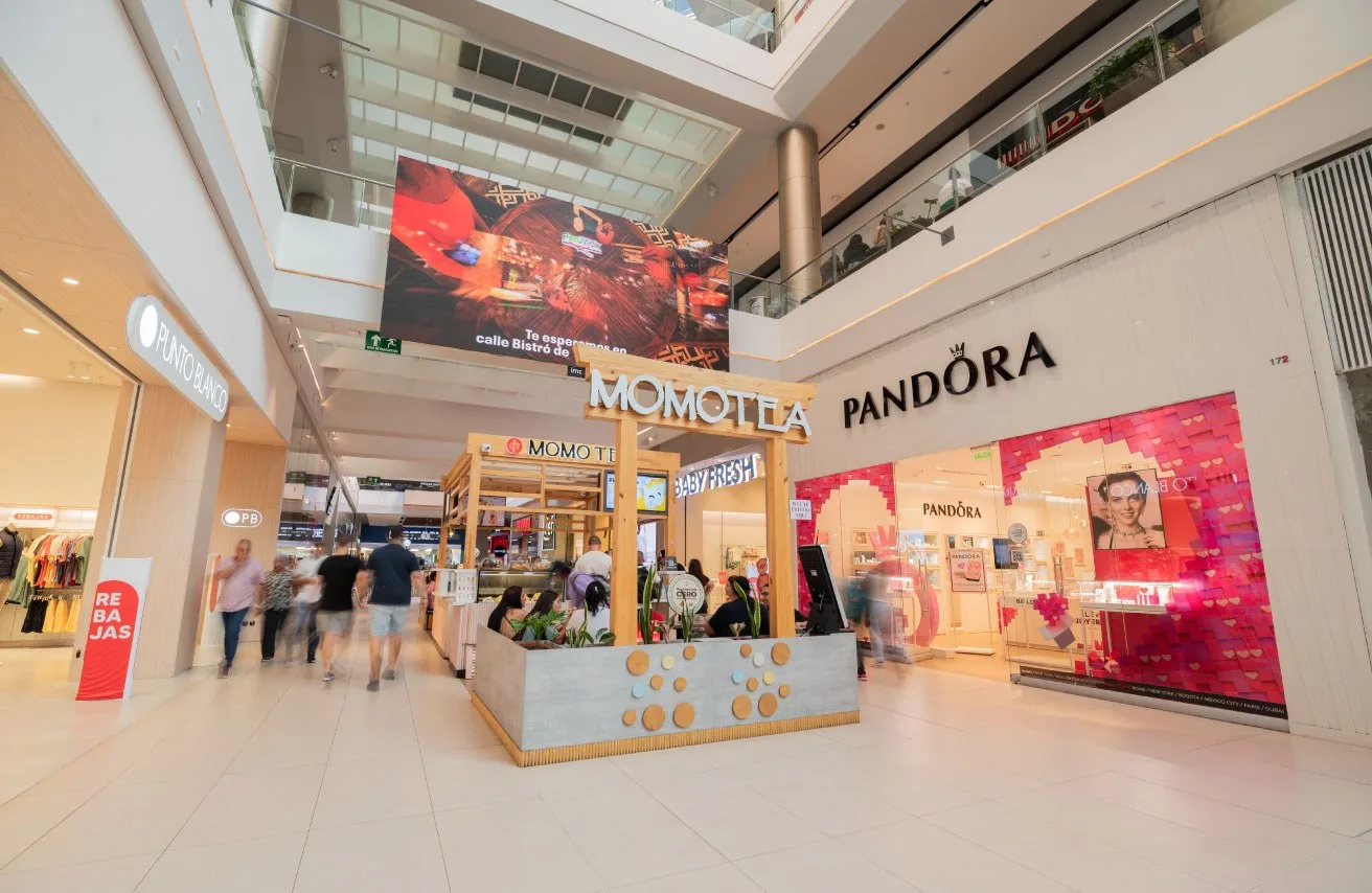 Pasillo interior del centro comercial con almacenes y un quiosco de bebidas